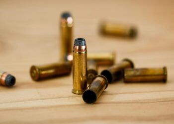 Detailed view of brass bullet shells scattered on a wood background.