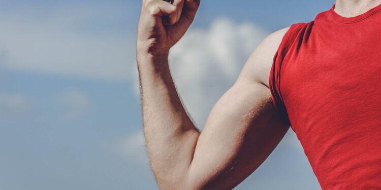 Close-up of a flexed arm in a red shirt against a clear blue sky, symbolizing strength and empowerment.