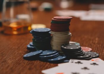 Poker chips and playing cards on a wooden table with a whiskey glass, emphasizing gambling and entertainment.