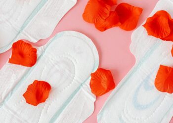 Close-up of sanitary pads with red petals on a pink background, symbolizing menstruation.