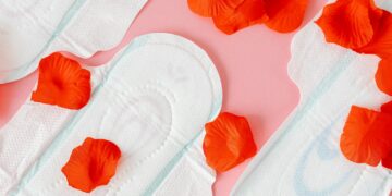 Close-up of sanitary pads with red petals on a pink background, symbolizing menstruation.