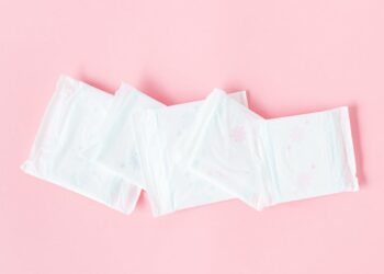 Minimalist shot of sanitary pads arranged on a pastel pink backdrop symbolizing feminine hygiene.