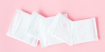 Minimalist shot of sanitary pads arranged on a pastel pink backdrop symbolizing feminine hygiene.
