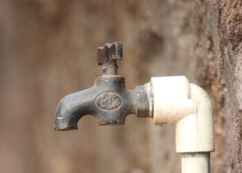 A close-up view of a rusty outdoor water tap attached to a wall, highlighting water scarcity issues.