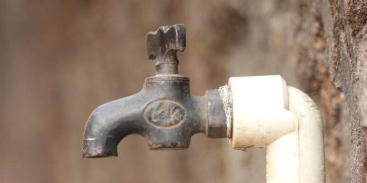 A close-up view of a rusty outdoor water tap attached to a wall, highlighting water scarcity issues.